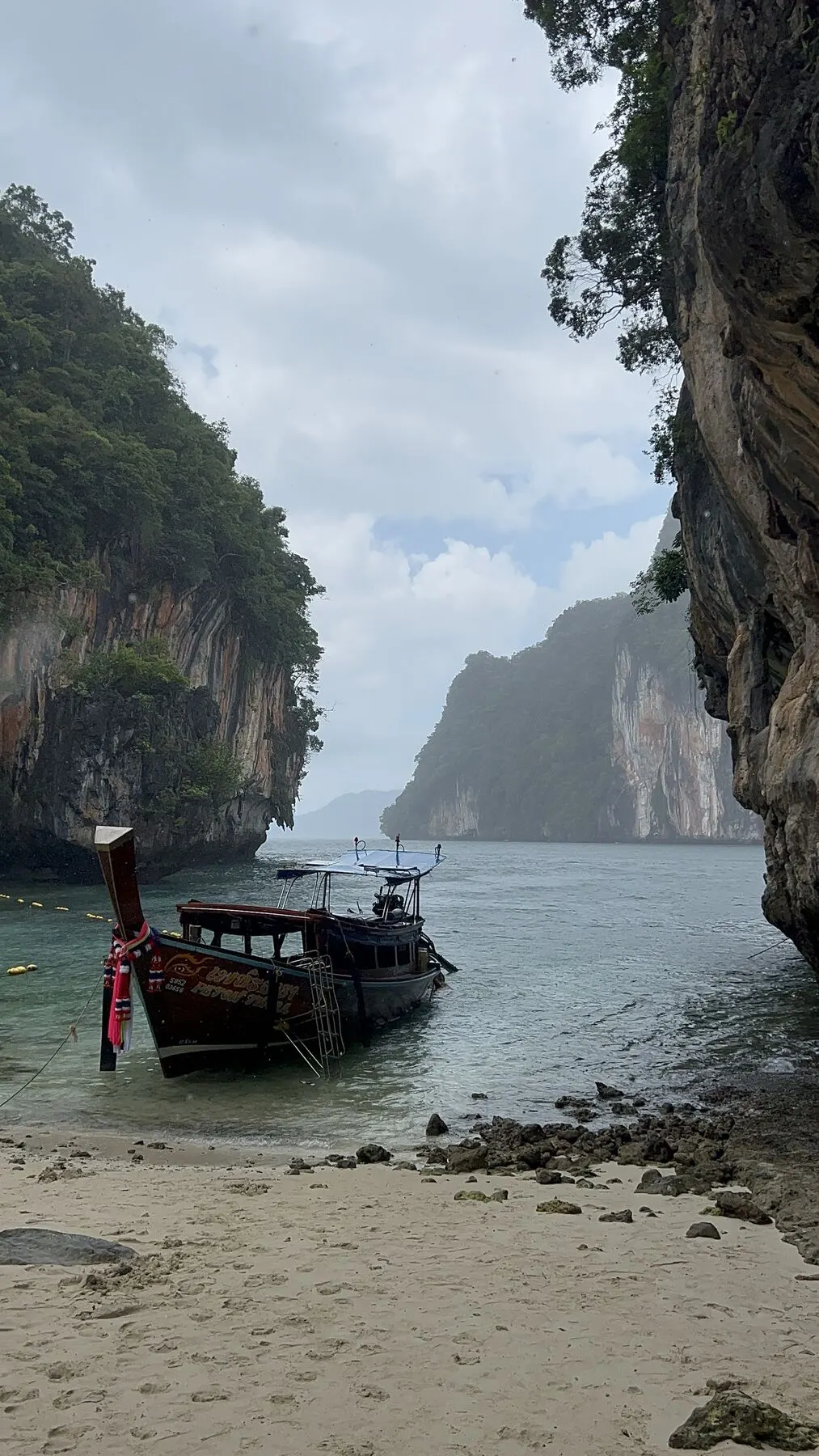 Longtail boat on a beach surrounded by cliffs, near Krabi